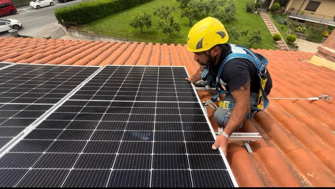 Un installatore con casco e imbracatura fissa un pannello fotovoltaico su un tetto in coppi