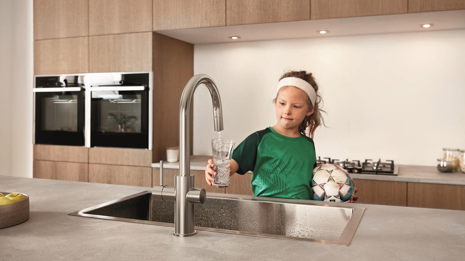 Bambina riempie un bicchiere d’acqua dal rubinetto della cucina
